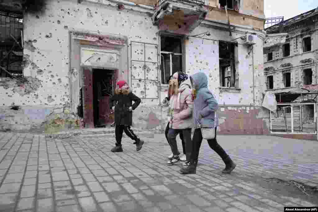 Дети проходят мимо посеченных осколками зданий в Мариуполе, 25 февраля 2023 года. Во время российской осады погибли тысячи мирных жителей города. Россия заявляет о 3000 убитых мирных жителях, а Украина – о более чем 25 000 погибших