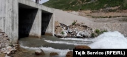 Vide se velika creva povezana sa ispusnim bazenima iz rudnika zlata Pokrud kako se napajaju u reku, odakle ispuštaju belo oticanje u vodu. (jun 2023.)