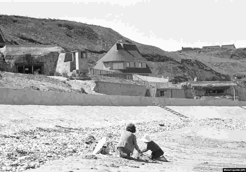 6 iunie 1964 - Copii francezi se joacă pe plaja din Vierville-dur-Mer - cunoscută sub numele de Omaha Beach - unde încă se aflau buncărele germane, la 20 de ani de la Ziua Z. De-a lungul celor 11 ani ca președinte al Franței, Charles de Gaulle a refuzat să participe la evenimentele de Ziua Z. A refuzat să comemoreze ziua de 6 iunie, având în vedere modul în care fusese tratat la momentul aterizării de Ziua Z. Nu fusese implicat în discuții sau în implementarea planului”, spune istoricul Denis Peschanski. De Gaulle nu a invitat nici liderii mondiali la cea de-a 25-a aniversare din 1969.