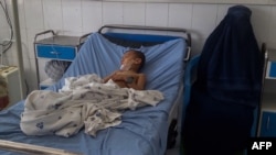 A burqa-clad Afghan woman sits next to a child receiving treatment at a hospital after he was injured in a bomb blast in Kunduz on April 21.