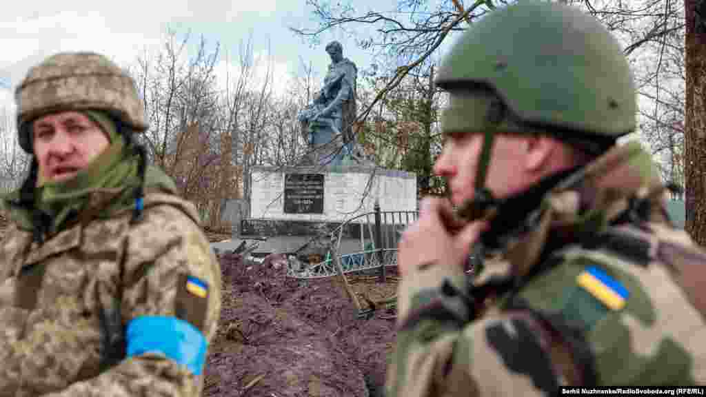 Українські військовослужбовці стоять біля пошкодженого меморіалу загиблим воїнам у Другій світовій війні у нещодавно звільненому селі Лук'янівка на Київщині, 27 березня 2022 року