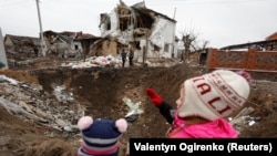 Діти дивляться на воронку, яка залишилася внаслідок російського ракетного удару в селищі міського типу Глевасі на Київщині, 26 січня 2023 року, ілюстративне фото