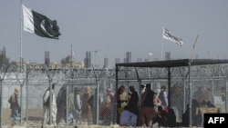 Afghan and Pakistani nationals walk through a security barrier to cross the border as the Pakistani and Taliban flags fly at the Pakistan-Afghanistan border crossing point in Chaman.