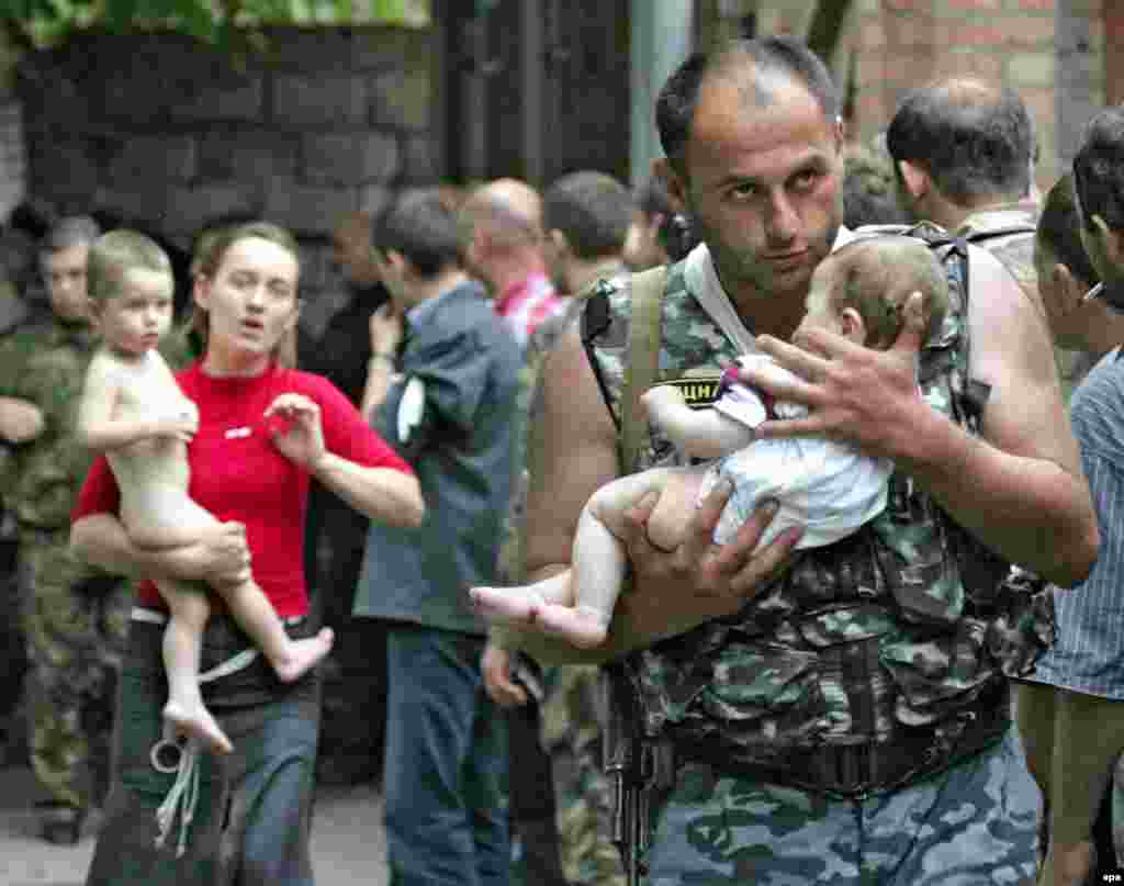 Представник силових структур виносить дитину – одну з 26 дітей і жінок, яких нападники випустили другого дня кризи. - Російські урядовці стверджують, що вбивати заручників почали захоплювачі, які підірвали вибухівку всередині школи. Але в Беслані багато хто каже, що бій спровокували силовики, вистріливши по школі з гранатомета. Через це провалився дах і почалася сильна швидка пожежа.