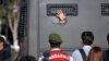 An Ergenekon prisoner being driven in a police armoured vehicle waves at protesters in August 2013 as police and gendarmerie block access to a courthouse in Silivri, near Istanbul.