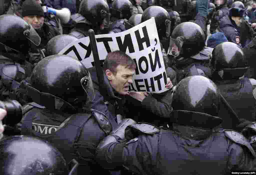 Російський ОМОН затримує протестуючого з плакатом із написом: «Путін, ти не мій президент» під час мітингу в Санкт-Петербурзі 28 січня. Мітинг «страйк виборців» був організований опозиційним діячем і борцем із корупцією Олексієм Навальним, який закликав своїх прихильників протестувати проти того, що його не допустили до участі у виборах президента Росії на підставі непогашеної судимості. Навальний був заарештований в Москві, оскільки викликані ним демонстрації проходили по всій країні. (AP/Dmitri Lovetsky)