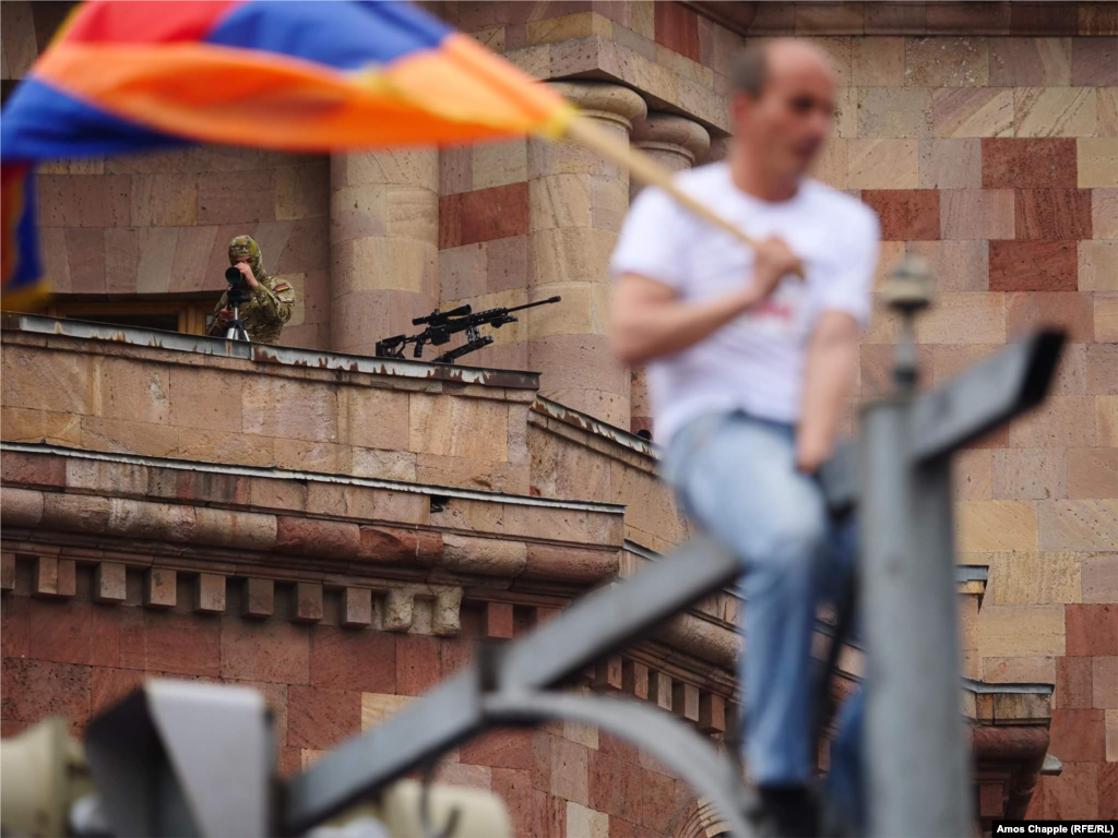 Снайпери в масках з гвинтівками на балконі будівлі уряду з видом на площу Республіки в Єревані, спостерігають, як десятки тисяч громадян зібралися для святкування «епохальної перемоги» на виборах лідера опозиції Ніколи Пашиняна. Вірменія, 8 травня. Фотограф Радіо Свобода/Радіо Вільна Європа Амос Чаппл згадує в інтерактивній історії «Caught Up In A Revolution», як він фотографував вуличні протести, які призвели до відставки прем’єр-міністра Сержа Саргсяна і його уряду (Амос Чаппл, Радіо Свобода/Радіо Вільна Європа)