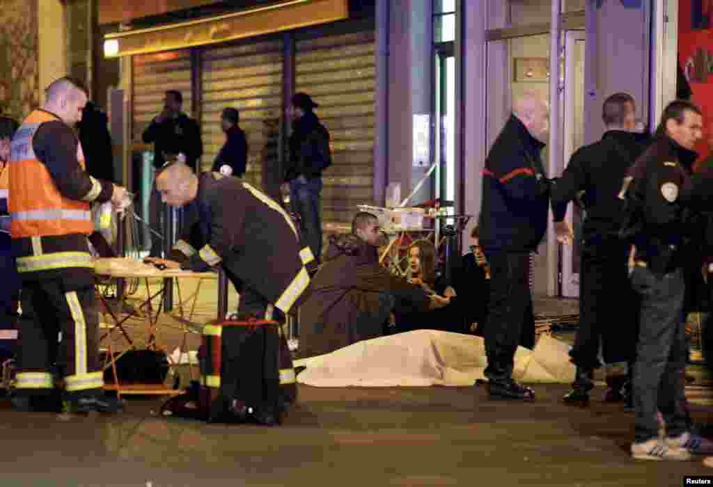 A French rescue worker checks his laptop computer as three people consol each other over the body of a shooting victim. 