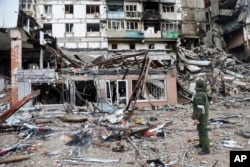 Un militar ucrainean priveșt o clădire avariată în timpul luptelor din Mariupol, Ucraina, 13 aprilie 2022.
