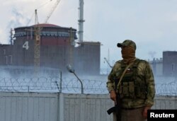 Un soldat cu steagul Rusiei pe uniformă stă de pază lângă centrala nucleară din Zaporojie. 4 august 2022.