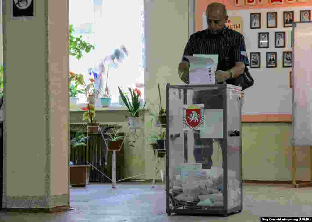 Мужчина кидает заполненные бюллетени в урну для голосования 