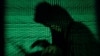 A hooded man holds a laptop computer as cyber code is projected - generic